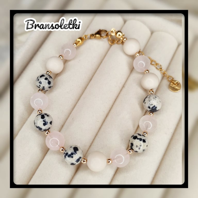 Bransolechi beaded bracelet with white ceramic beads, rose quartz, and blue-white spotted accent beads on gold hardware, displayed on cream fabric