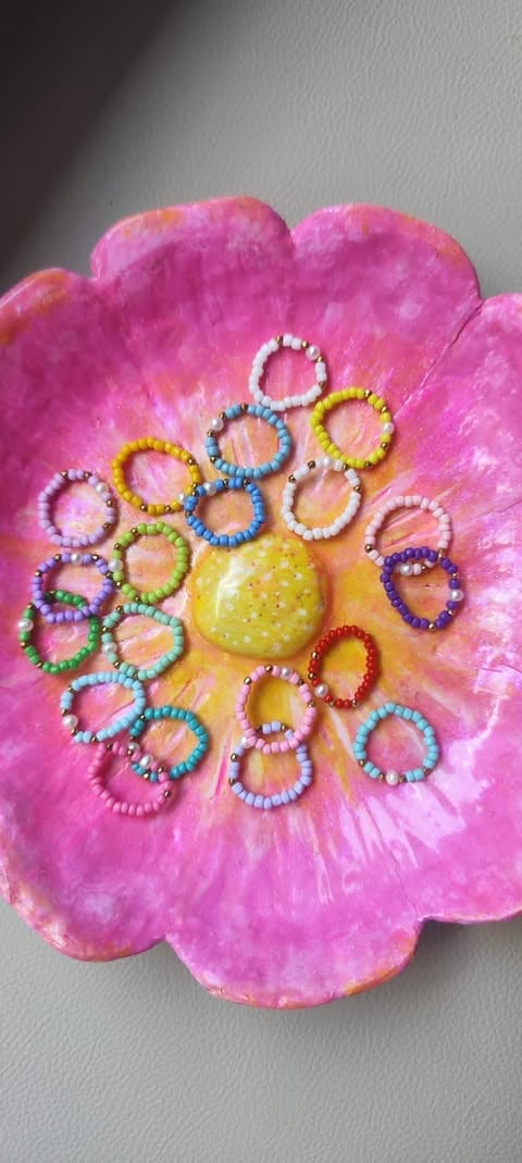 Bright pink flower-shaped craft with colorful beaded rings arranged around a yellow center bead on white surface