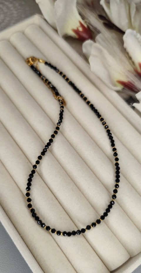 Black beaded necklace with gold clasps displayed on white ridged jewelry holder with flower petals