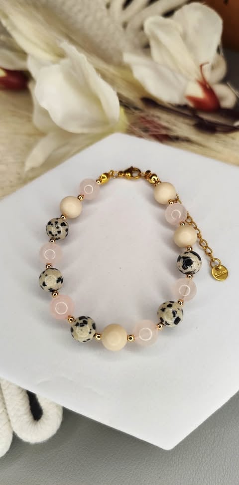 Beaded bracelet with cream, rose quartz, and spotted Dalmatian beads on white dish with white flowers